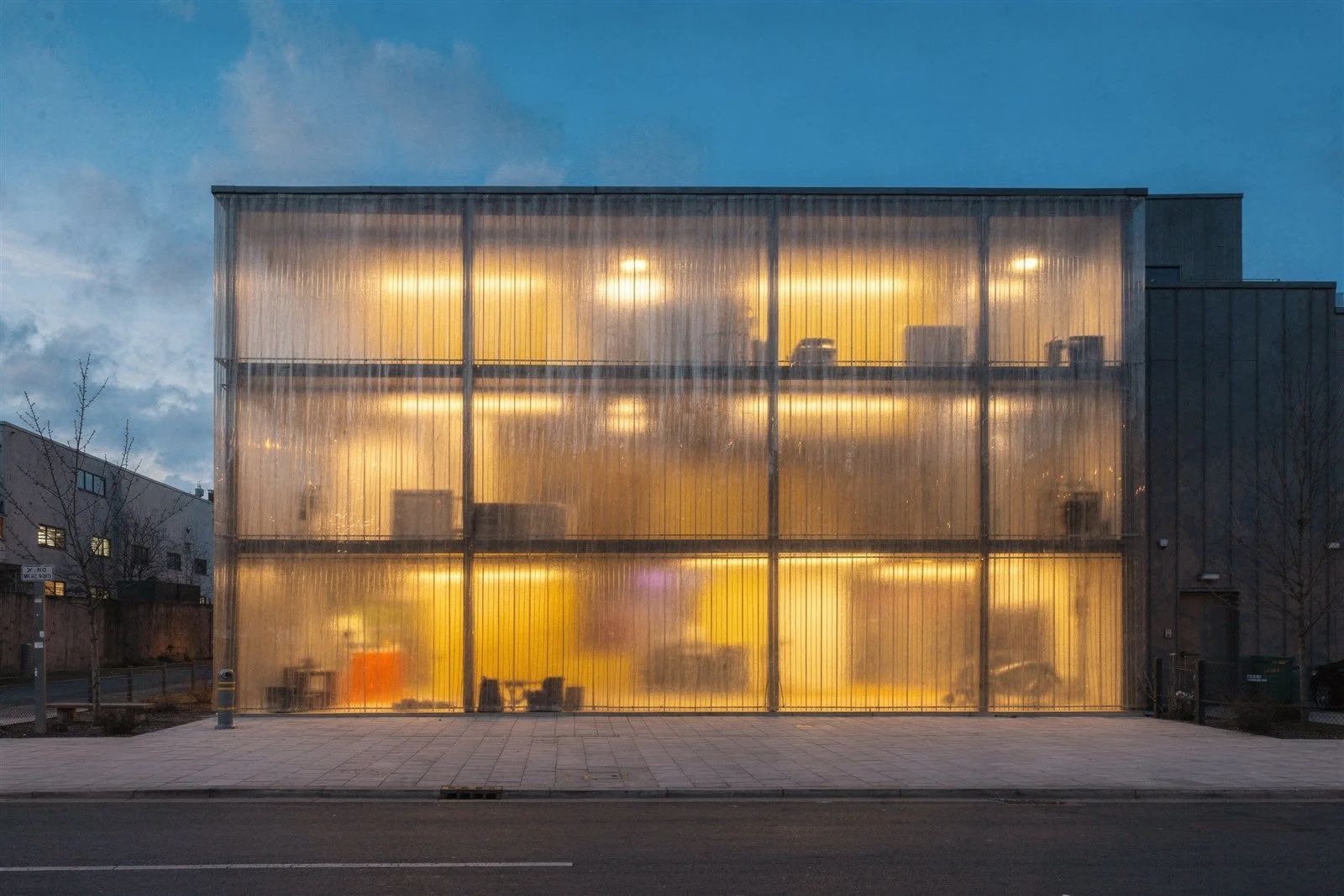 AI-generated architectural photograph of a warehouse conversion with a translucent polycarbonate facade glowing at dusk